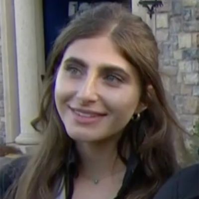 Shanel Naoum is looking at something as she is rocking her long brown hair and is also wearing a necklace.